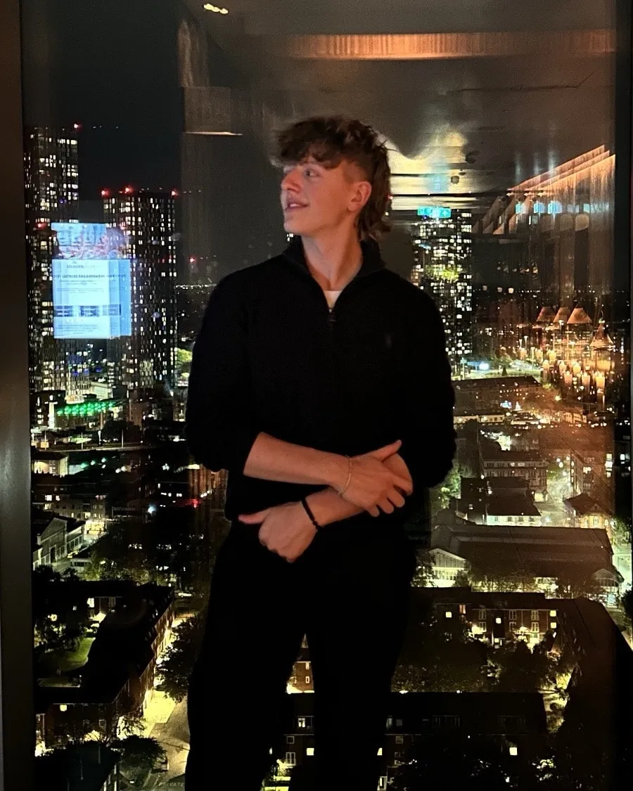 Mason Cowley by a window at night, with a city skyline behind him